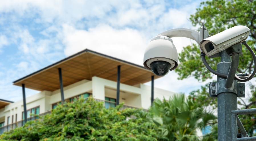 corner of a business building in the background with trees and a commercial security camera in the foreground.