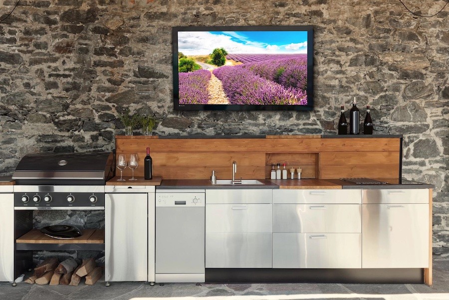 outdoor TV mounted above an outdoor kitchen area with grill, sink, and cabinetry