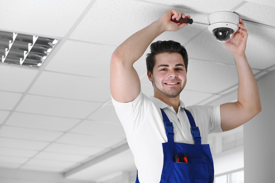 Image is of a commercial AV installer hanging a camera on the ceiling.