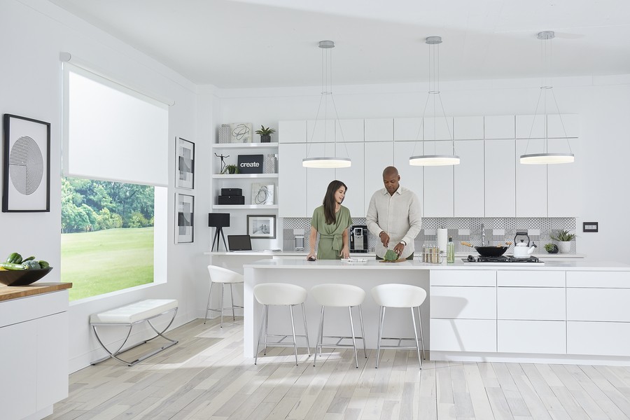 Two people in a kitchen cooking. Legrand shades are partially lowered over the window. 